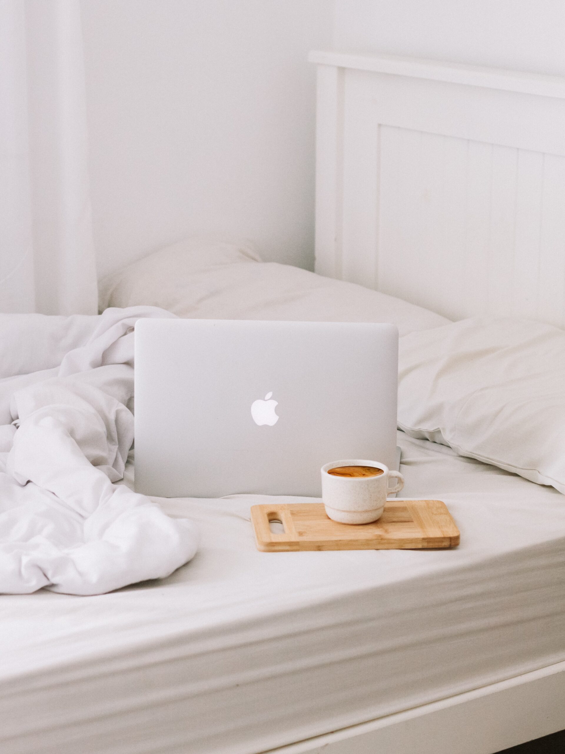 Laptop and coffee on a white bed and white duvet
