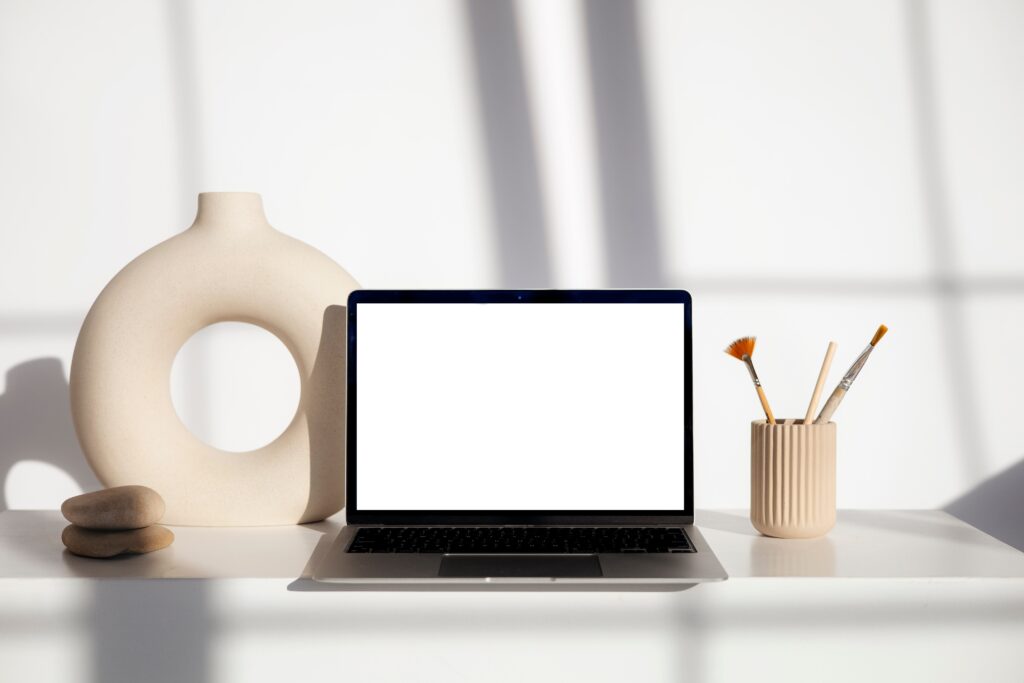 Open laptop with email marketing for coaches and a beige circular vase and a pencil holder