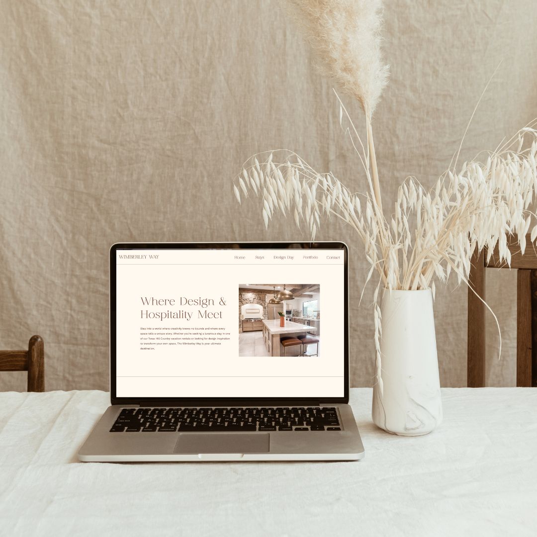 Interior design website on a laptop with a linen backdrop, linen table cloth and a vase with white fauna.