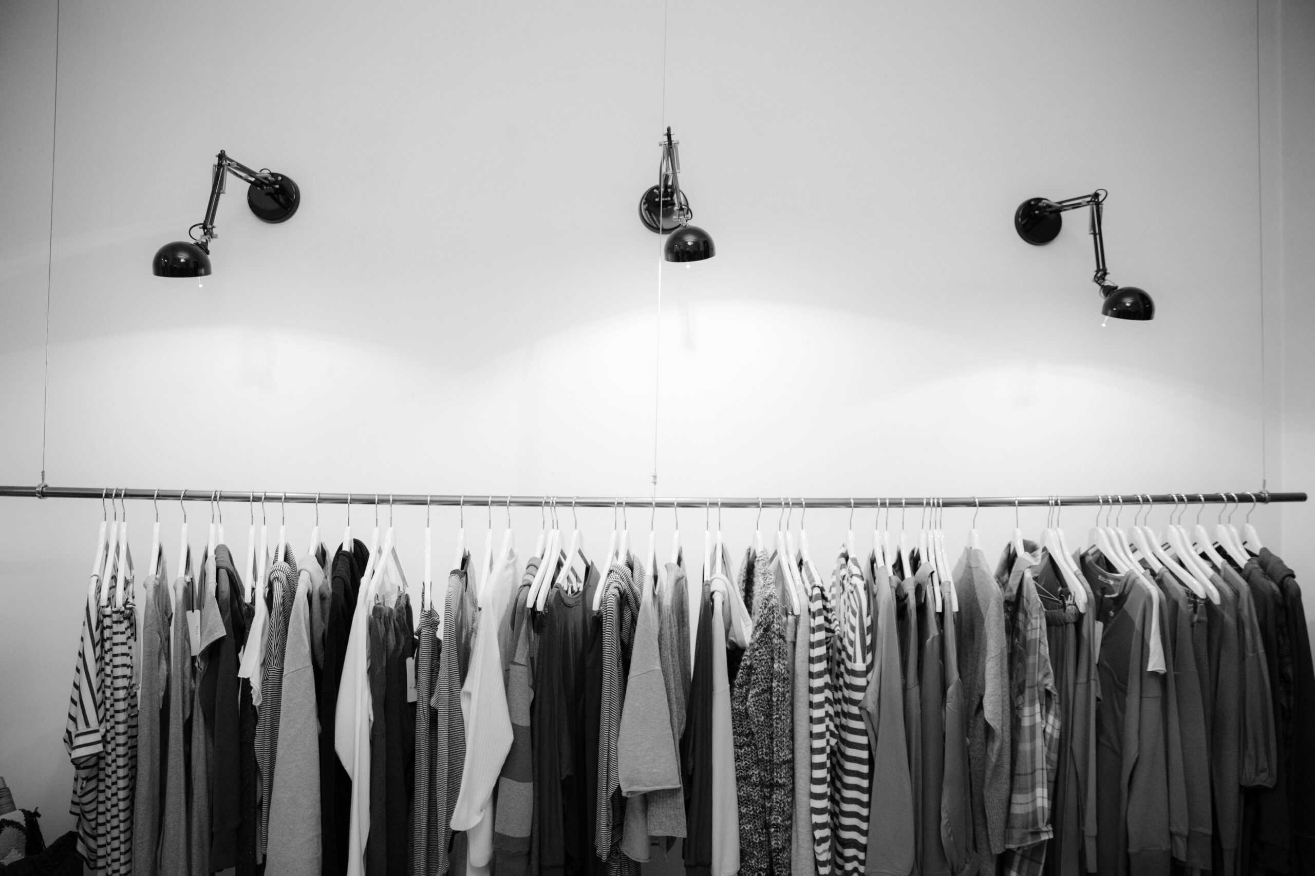 Shopify store with clothes hanging on a rack with lights shining on them. Image is in black and white.